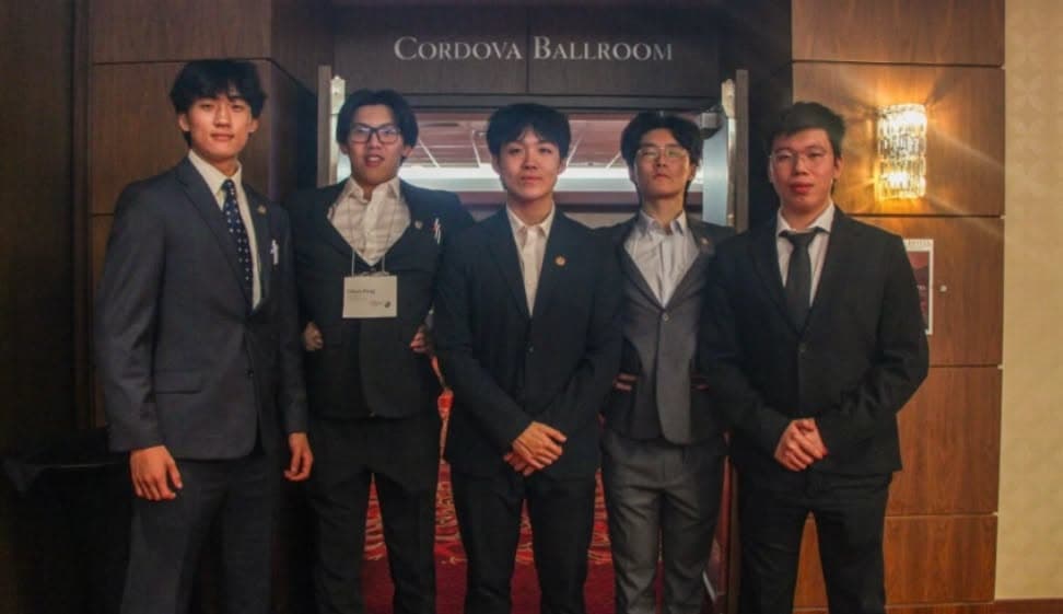A group in formal clothes with a plaque outside a ballroom during an IB Director event